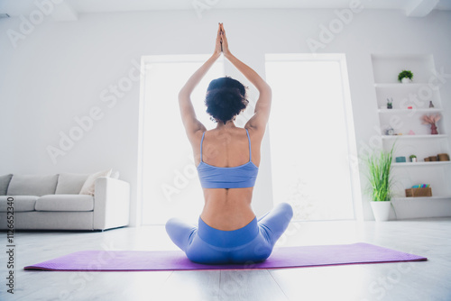 Young woman practicing yoga on purple mat indoors in sunny room for wellness and calm