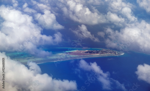 Aerial view from airplane window of Male, Maldives in scattered fluffy clouds layers. High flight of plane over blue sea and island with beach, coral reef. Scenic cloudscape and tropical climate