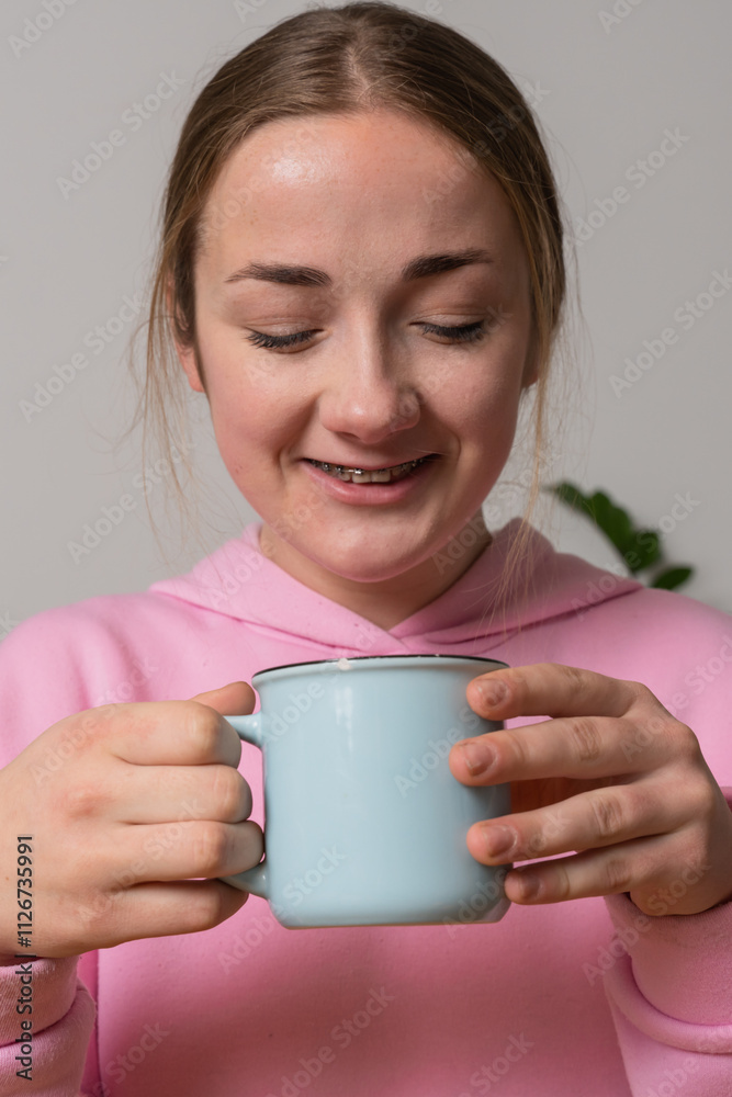 Young girl with braces holds cup with tea at the kitchen Young girl with braces holds cup with tea at the kitchen