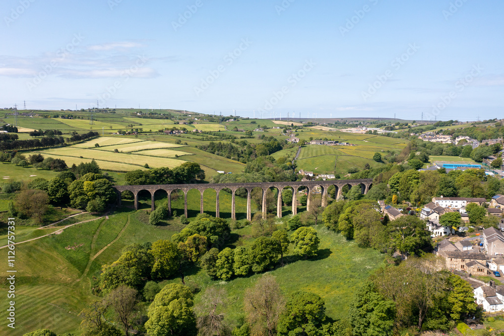 Obraz premium Aerial drone photo of the town of Thornton which is a village within the metropolitan borough City of Bradford in West Yorkshire, England showing the village and famous viaduct in the summer time.