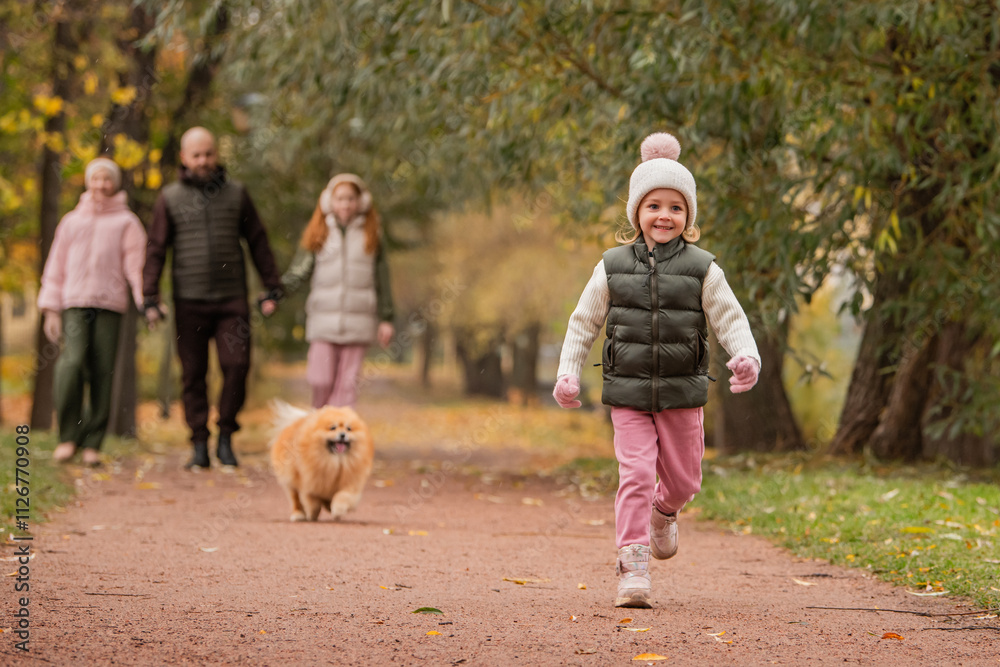 Obraz premium A little girl and her pet Pomeranian run along a path in an autumn city park.