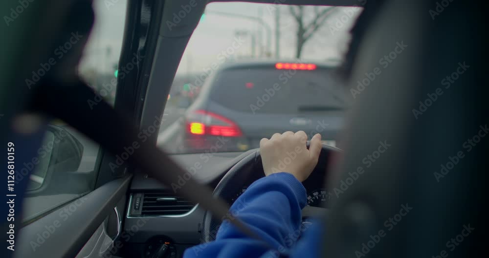 A view inside a car shows hands gripping the steering wheel while watching the traffic ahead A view inside a car shows hands gripping the steering wheel while watching the traffic ahead