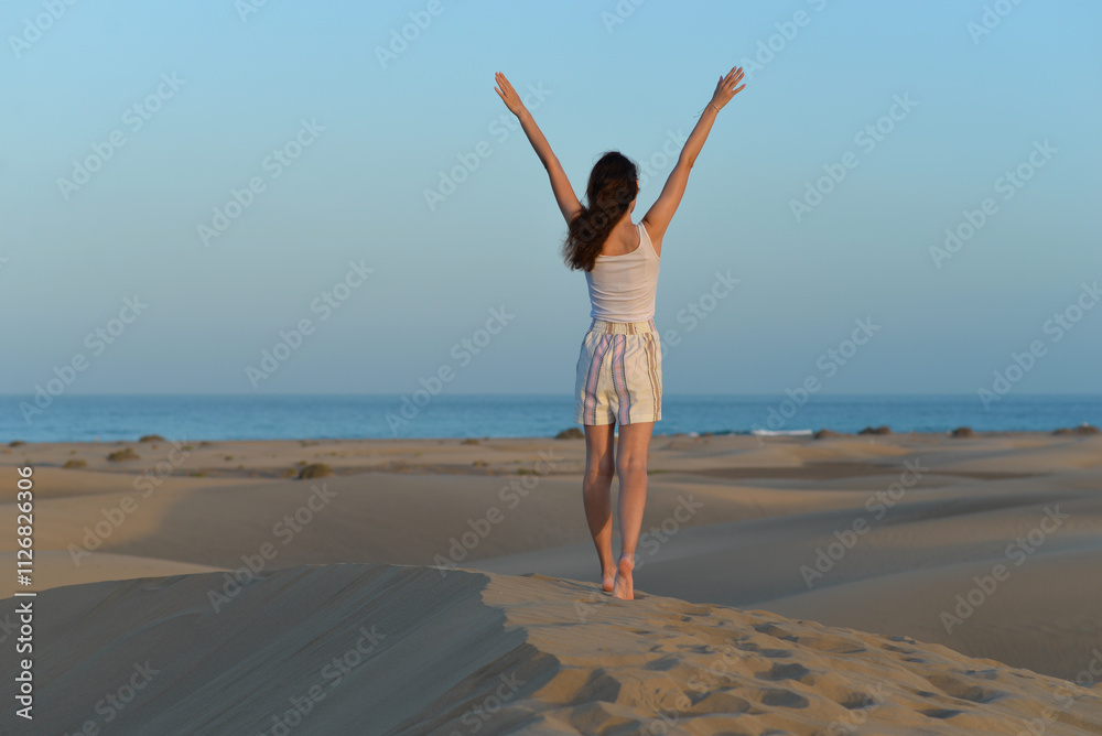 A girl walks along the sand against the background of the sea, rear view at a golden hour before sunset. Dune in Maspalomas, Gran Canaria. Touristic travel concept A girl walks along the sand against the background of the sea, rear view at a golden hour before sunset. Dune in Maspalomas, Gran Canaria. Touristic travel concept