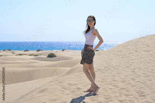 A girlstanding in a model pose on the sand at the background of the sea. Dune in Maspalomas, Gran Canaria. Touristic travel concept photo