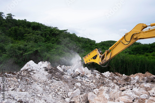 Excavator breaking and drilling stone in quarry. Large pneumatic jack hammer mounted on the hydraulic arm. photo