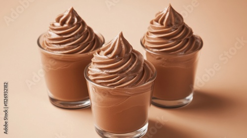 Three glasses of chocolate mousse with swirled peaks arranged on a beige background