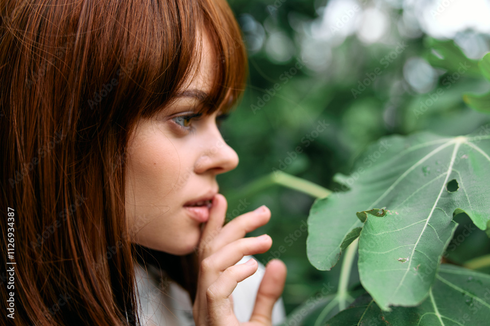 Woman in awe of intricate leaf while standing beside lush green plant Woman in awe of intricate leaf while standing beside lush green plant