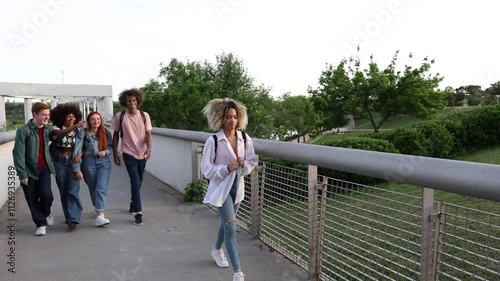 Group of teenagers laughing and pointing while walking behind a lone student on a bridge, highlighting peer pressure and bullying in a school setting photo