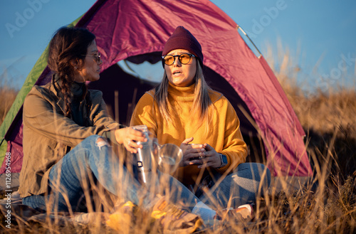 Two women camping at top of the hill sitting in front of the tent resting after hiking. photo