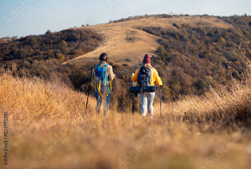 Rear view two woman hiking at top of the hill at meadow.