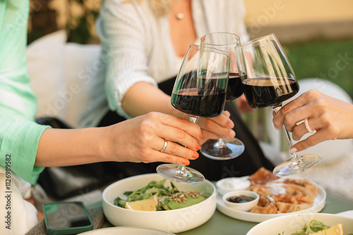 Close-up of three women having lunch outdoors making a celebratory toast with glasses of red wine photo