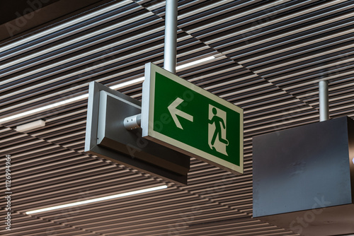 View on emergency exit sign. With running figure and arrow to the left. Neutral, white background. Modern design. Hanging from the ceiling. photo