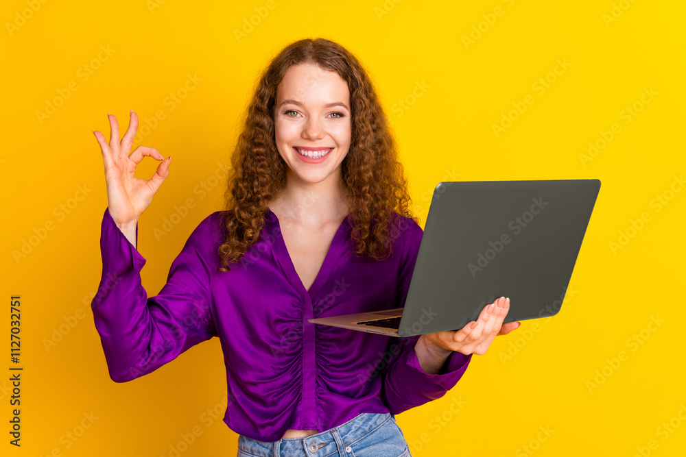 Photo portrait of attractive young woman hold netbook show okey dressed stylish violet clothes isolated on yellow color background Photo portrait of attractive young woman hold netbook show okey dressed stylish violet clothes isolated on yellow color background