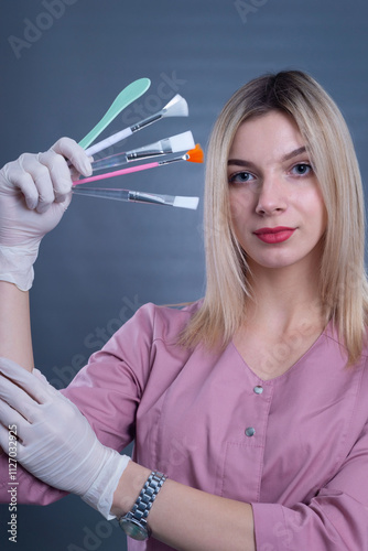 a young girl doctor holds cosmetic brushes for skin procedures in her hands. On a gray background