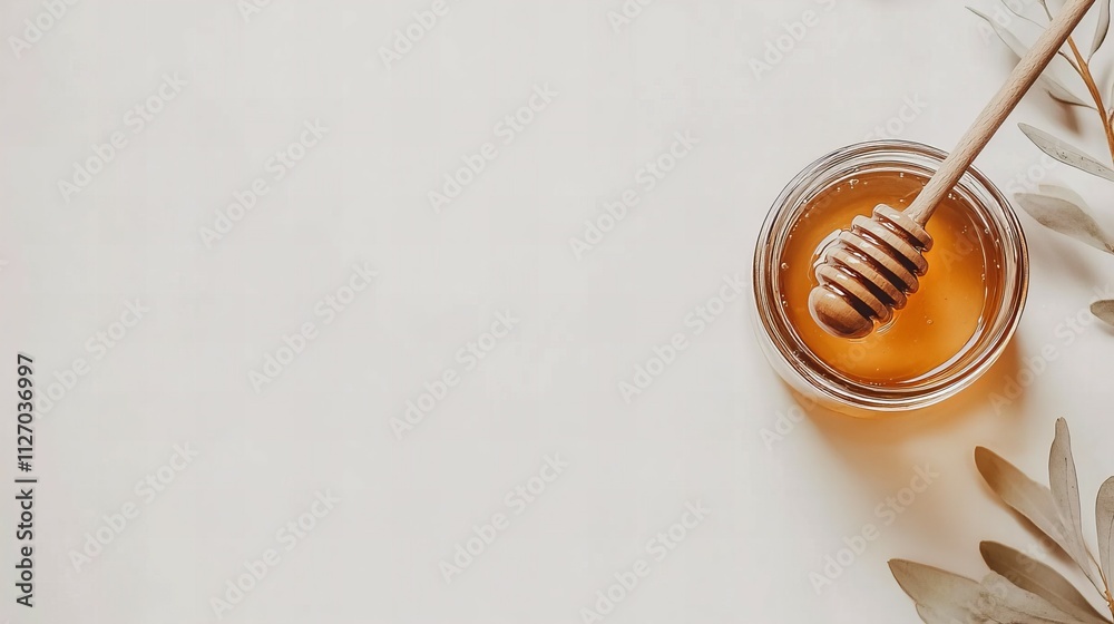 Fototapeta premium A glass jar filled with golden honey, a wooden honey dipper resting inside, set on a pristine white background for natural food themes 