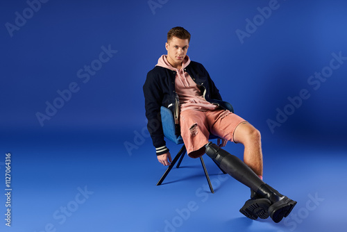 Young man poses confidently while seated, showcasing his stylish attire and prosthetic leg. photo