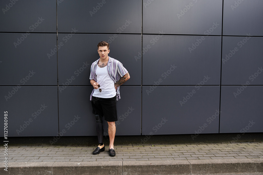 Young man with a prosthetic leg leans against a modern wall, exuding style and confidence. Young man with a prosthetic leg leans against a modern wall, exuding style and confidence.
