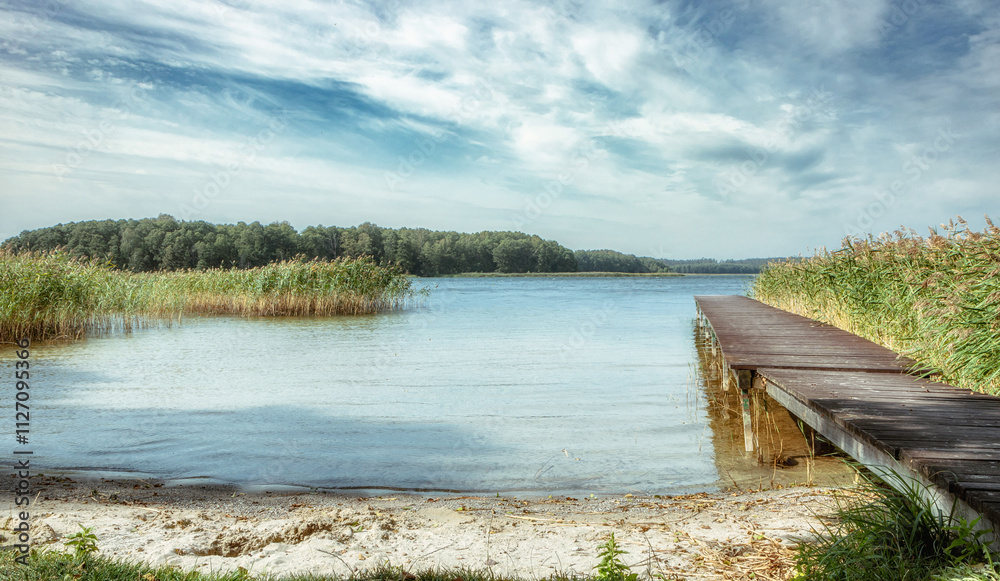 Fototapeta premium Beautiful, deserted beach and jetty in Poland in midsummer. Lonely idyll without people in the great outdoors. Wooden pier on the beach and pier for boats. Fantastic nature in deserted paradiese.