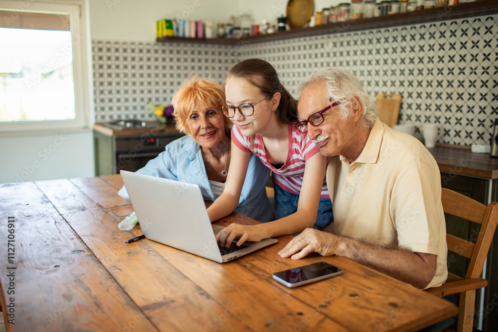 Teen girl using laptop with grandparents watching on kitchen table Teen girl using laptop with grandparents watching on kitchen table