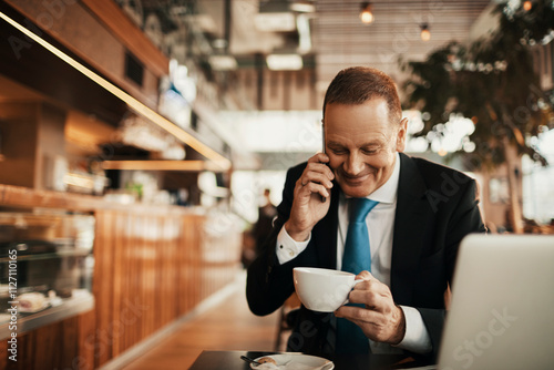Focused businessman working on laptop while drinking espresso in a busy cafe
