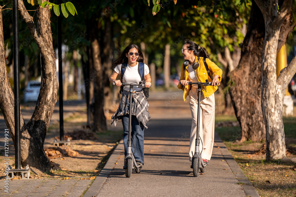 Fototapeta premium Two women riding scooters down a sidewalk