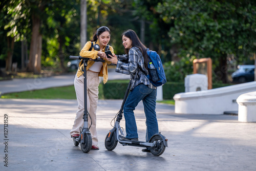 Two women are riding scooters and one of them is holding a cell phone photo