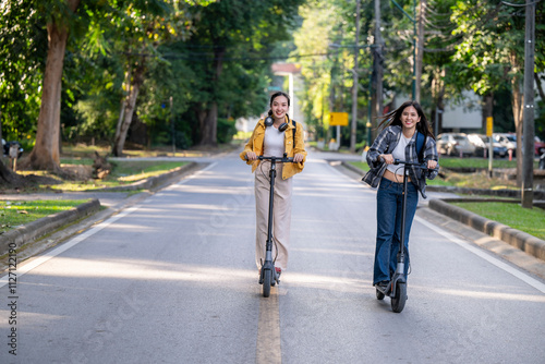 Two women riding scooters down a street