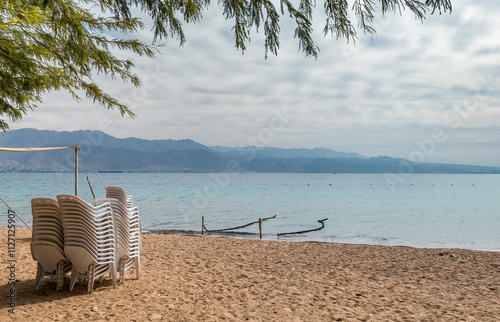 Morning on sandy beach with sunshades of trees branches, unpacked resting dec...