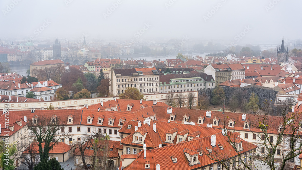 Obraz premium Panoramic view of the city of Prague with its old buildings and red roofs on a day of thick fog.