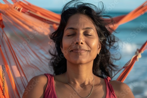 Portrait of a blissful indian woman in her 40s showing off a lightweight base layer over relaxing hammock on the beach background photo