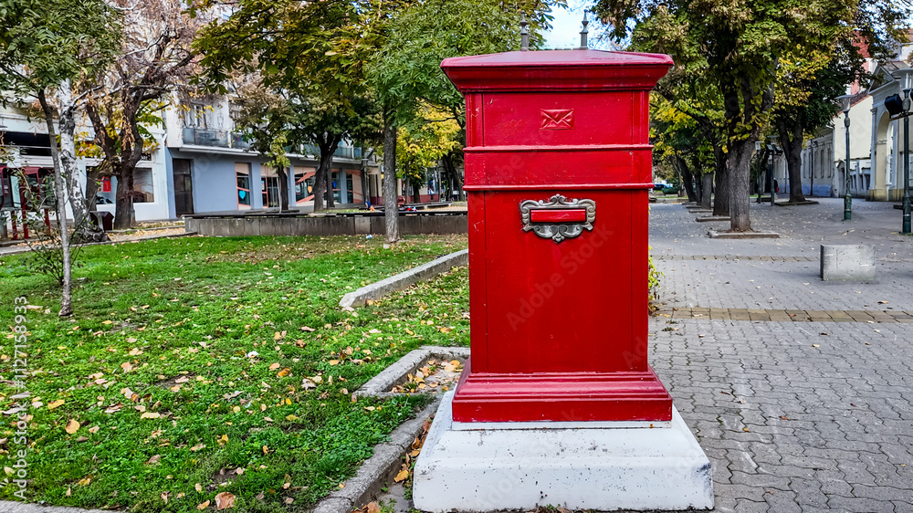 A vibrant red British-style postbox stands on a tree-lined city street, symbolizing communication and nostalgia A vibrant red British-style postbox stands on a tree-lined city street, symbolizing communication and nostalgia