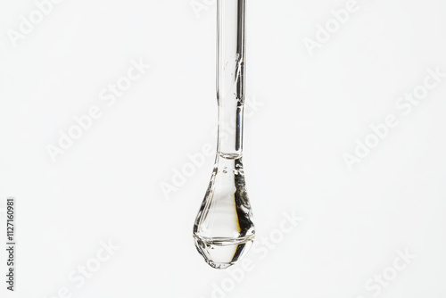 A clear liquid droplet hanging from a pipette against a white background. photo