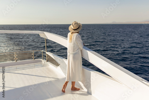 Elegant sexy woman in white dress standing near railings and looking on sunset. Like yacht style.