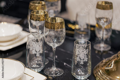 A beautifully arranged table features intricate glassware with gold accents alongside high quality dishware, ready for a memorable dining experience. Serving glassware and dishware for new year party photo