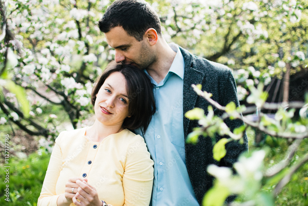 husband and a pregnant wife hug in a spring garden surrounded by blossoming apple trees husband and a pregnant wife hug in a spring garden surrounded by blossoming apple trees