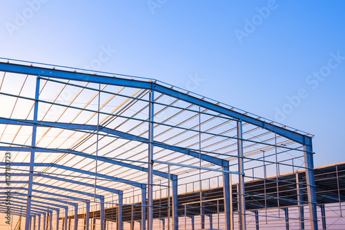Factory building framework with metal post and roof beam structure  in construction site against evening sky background, low angle view