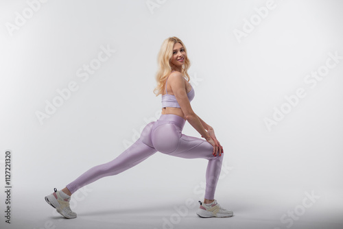 Fashion beautiful young woman model with smile in fashionable sportswear with top and leggings with sneakers warming up and stretching legs on gray background