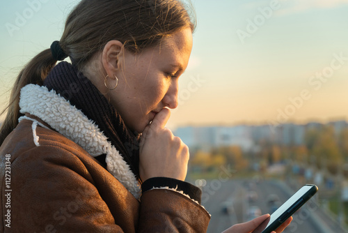 Foto Young woman lost in thought, biting her finger, engrossed in her smartphone at s