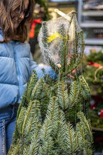 Young woman with blue jacket buying Christmas tree from market
