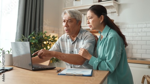 Grandmother comforting and encouraging senior smart manager working and pointing at laptop showing deceasing financial chart. Elder couple helping and talking together while sitting at home. Myrmidon.