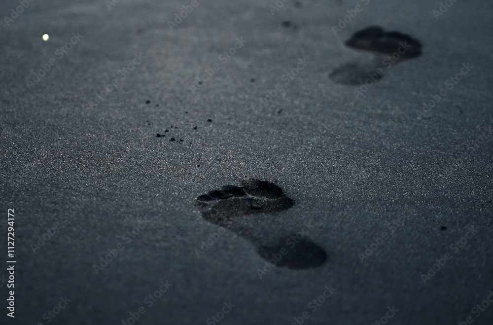 A black volcanic sand on a beach closeup with a person footprints. A black volcanic sand on a beach closeup with a person footprints.