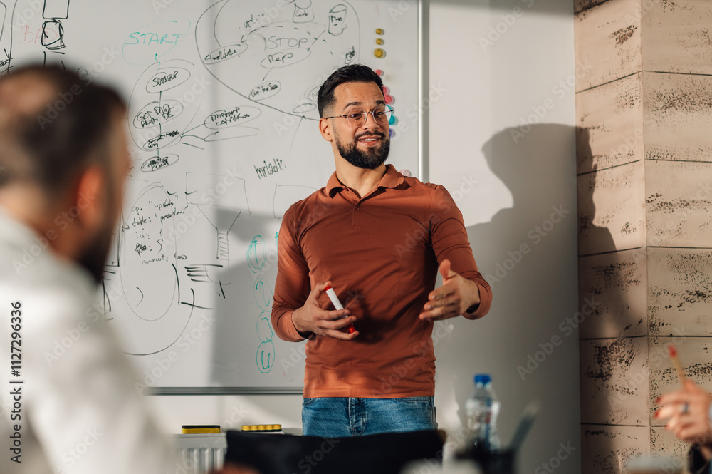 Confident male project manager leading a presentation to coworkers in meeting room Confident male project manager leading a presentation to coworkers in meeting room