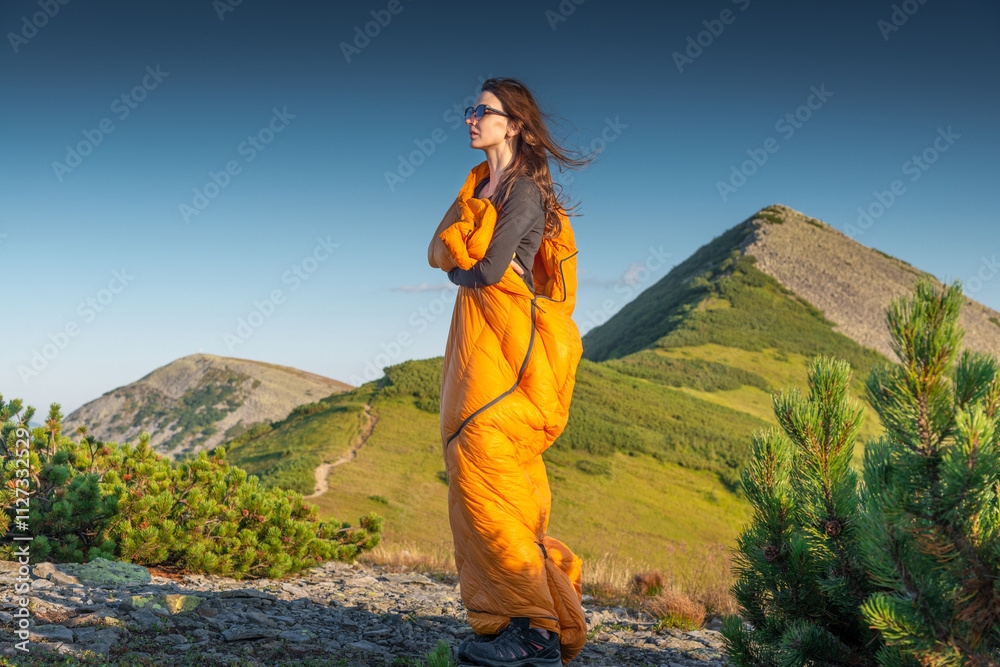 Naklejka premium Woman in orange sleeping bag enjoying sunset in mountains