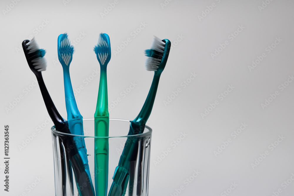 Glass with four toothbrushes in it. Toothbrush with gray glass background. Man is putting brush on glass and a gray background. A white toothbrush with gray brushes and a gray background lifestyle.