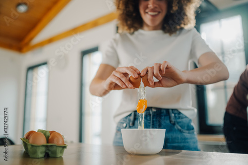 Woman cracking eggs into bowl in kitchen, preparing ingredients for baking photo