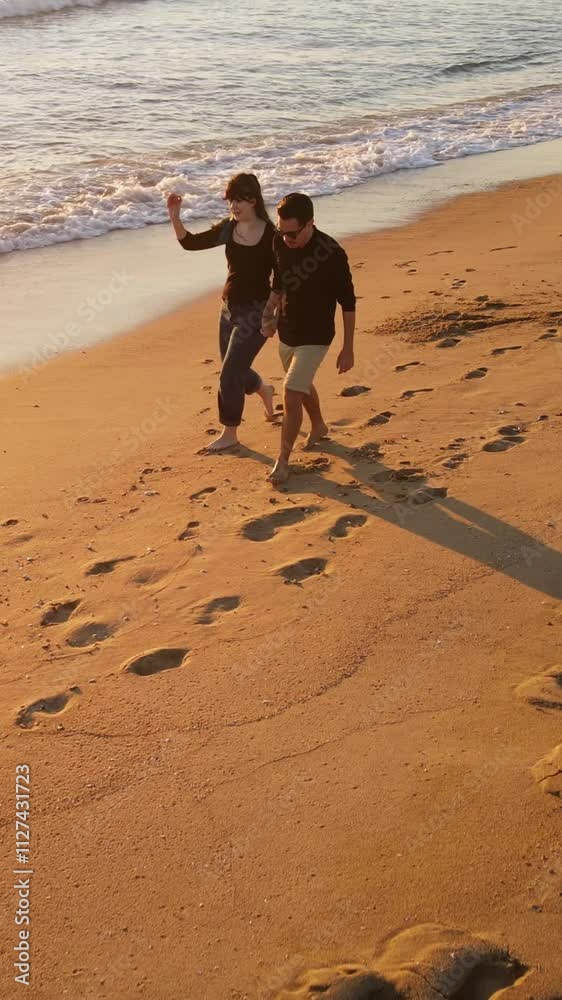 Aerial shot of a happy couple walking on the beach at sunset in Southern California. Vertical Video.