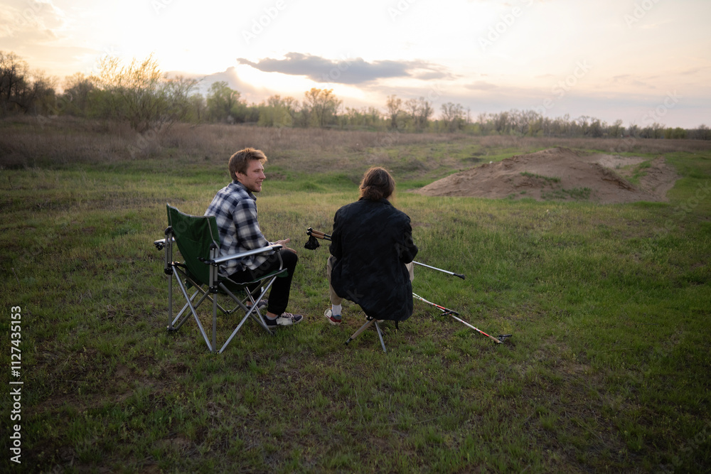 Two friends relax while hiking, enjoying nature and catching their breath on a grassy area under a cloudy sky Two friends relax while hiking, enjoying nature and catching their breath on a grassy area under a cloudy sky