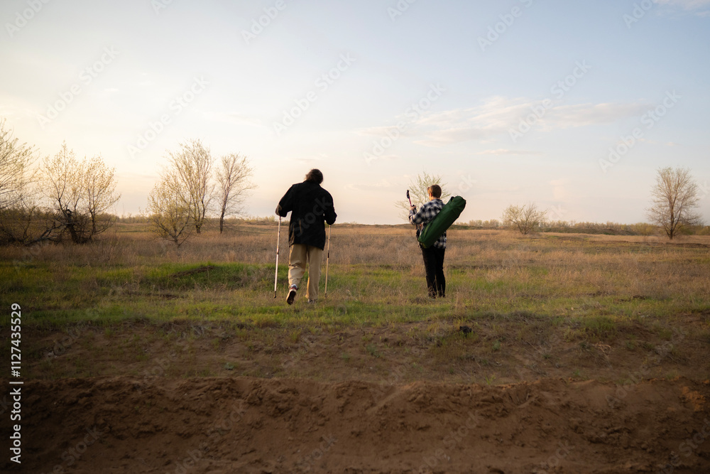 Two hikers walk along a dirt path in a nature field, enjoying the beauty of a sunset on a calm evening Two hikers walk along a dirt path in a nature field, enjoying the beauty of a sunset on a calm evening