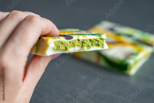 Piece of trend Dubai white chocolate with pistachio paste and kataifi dough in woman hand. Confectionery handmade sweets at home in the kitchen.  photo