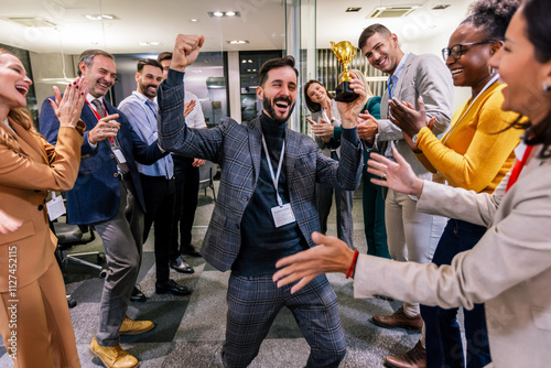 Young businessman receiving prize cup, proud colleagues applauding for him and cheering. photo